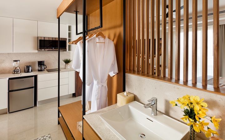 Luxury bathroom and dressing area showcasing a sleek washbasin vanity alongside plush hanging bathrobes and an open closet wardrobe for garment storage at Kadun Hotel Boutique.